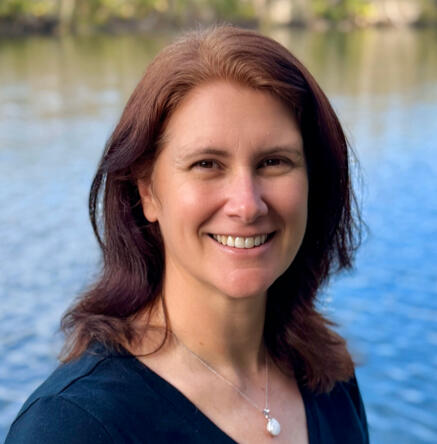Headshot of ghostwriter and freelance writer, Karen McLaughlin. A woman with shoulder length brown hair, wearing a black shirt, standing in front of a lake.